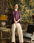 Woman standing in a room with decorative wall tapestry and vintage furniture.