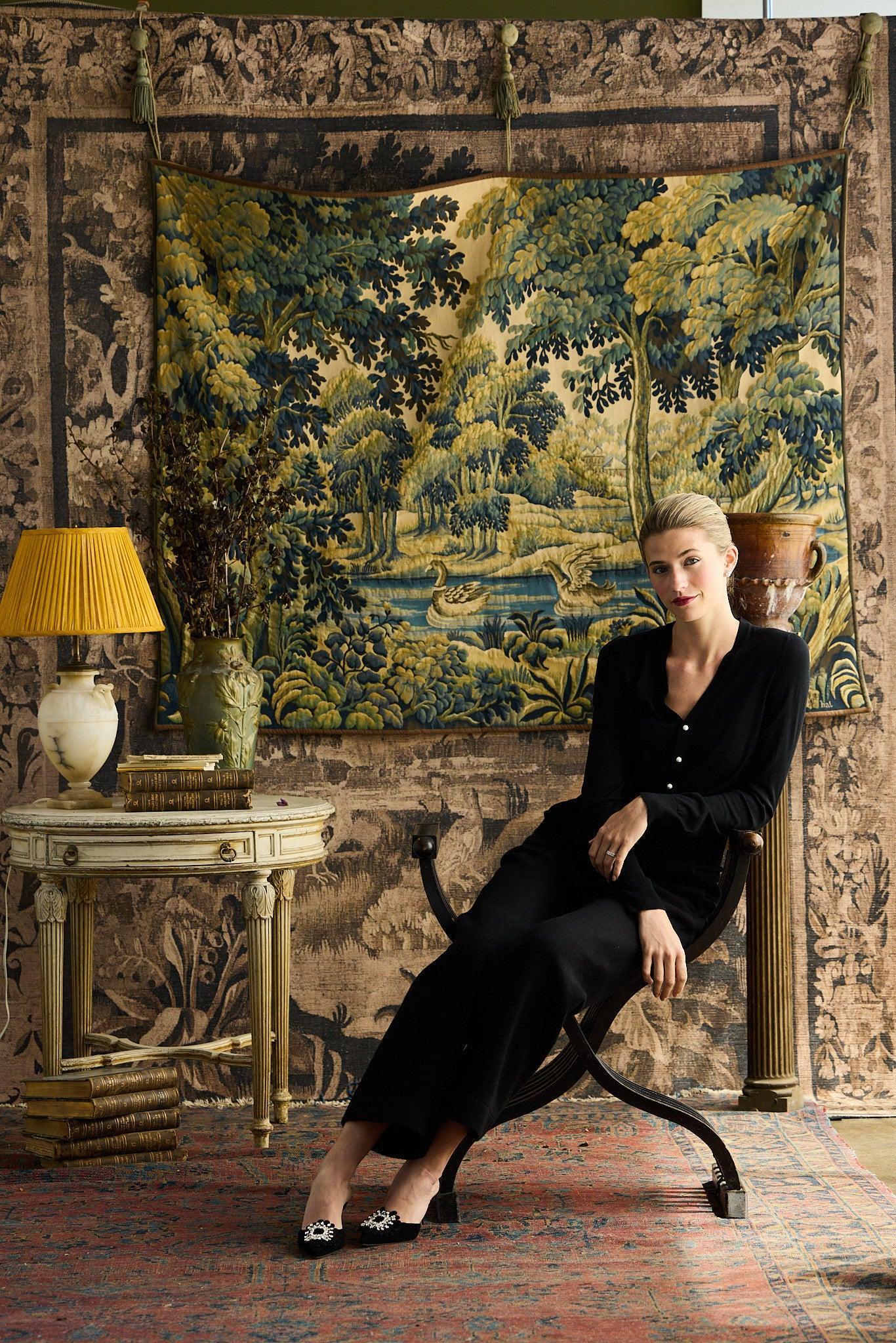 Woman sitting in a chair in a room with a large tapestry on the wall.
