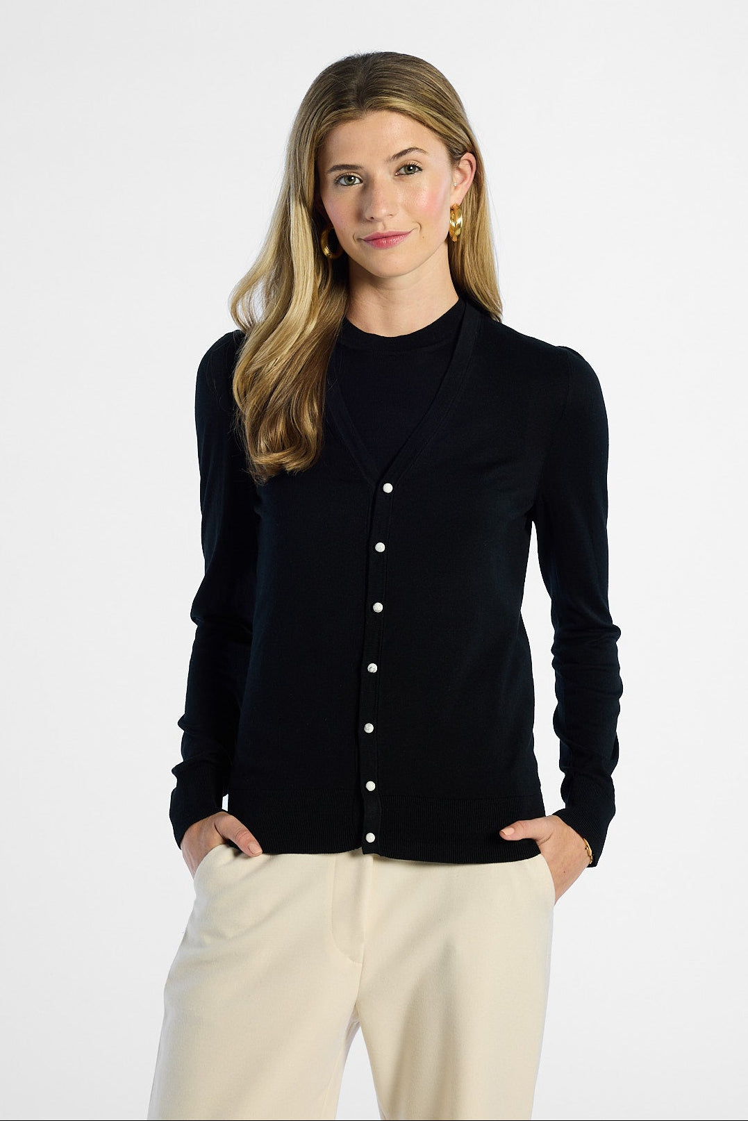 Woman wearing a black button-up cardigan and beige pants on a white background