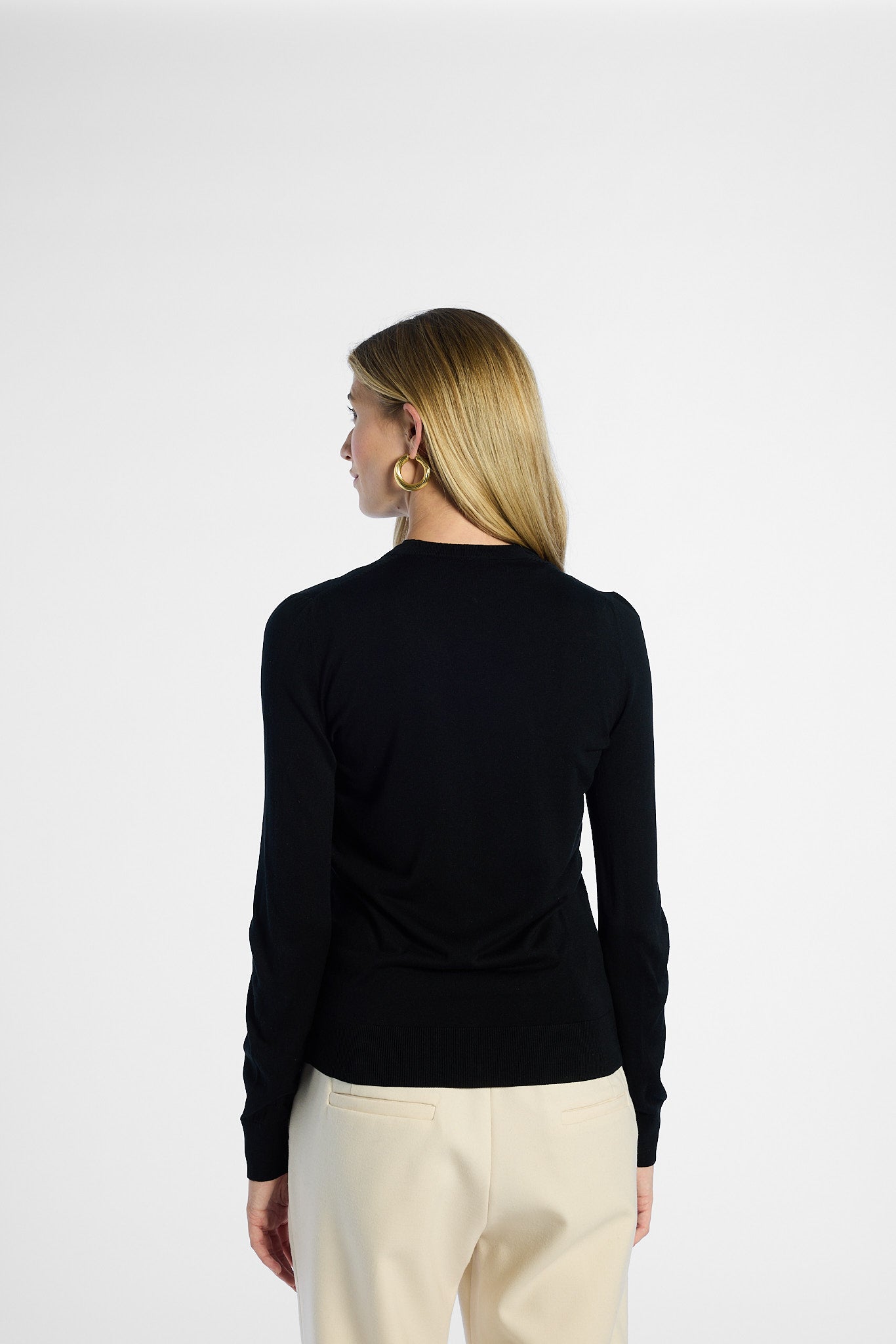 Back of woman wearing a black silk cardigan and beige pants on a white background