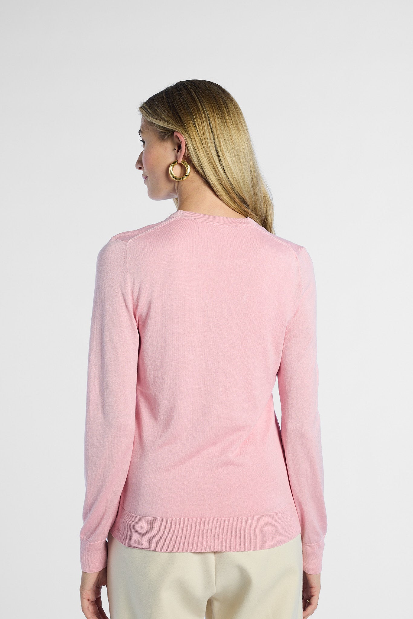 back profile shot of a woman wearing a pink silk cardigan against a white background
