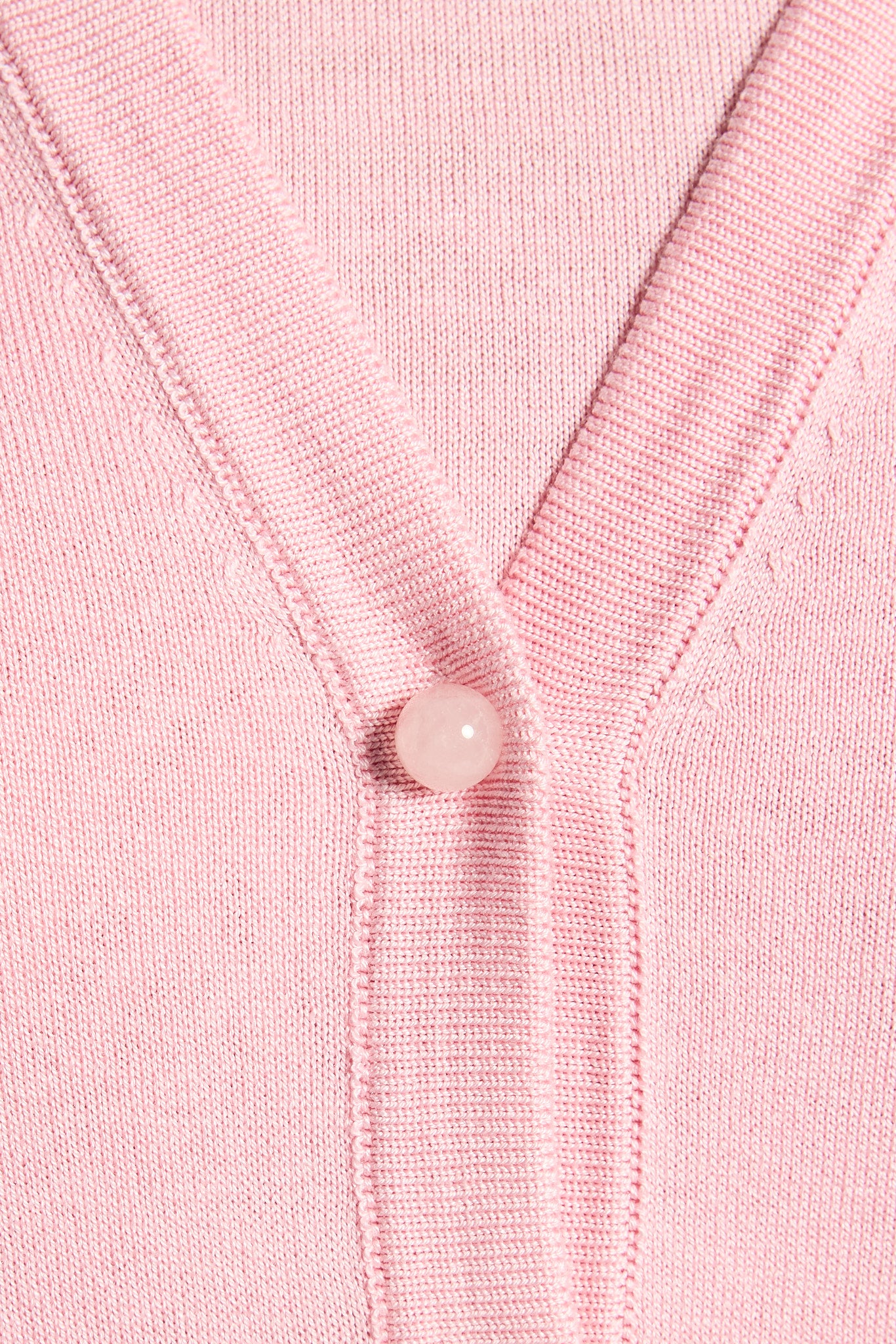 Close-up of a pink cardigan with a gemstone button on a matching pink background