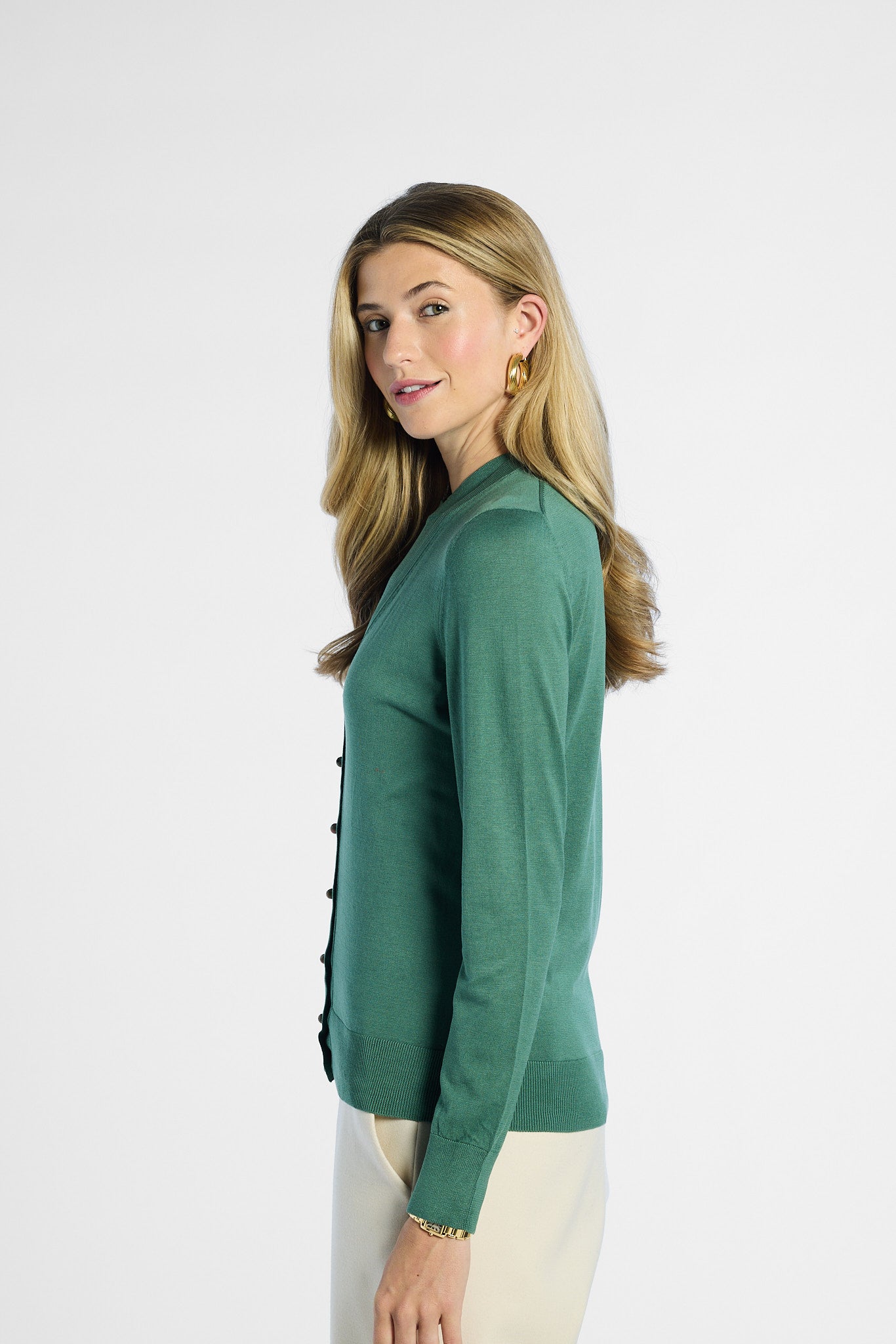 side profile of a woman wearing a green sweater with black buttons on a white background