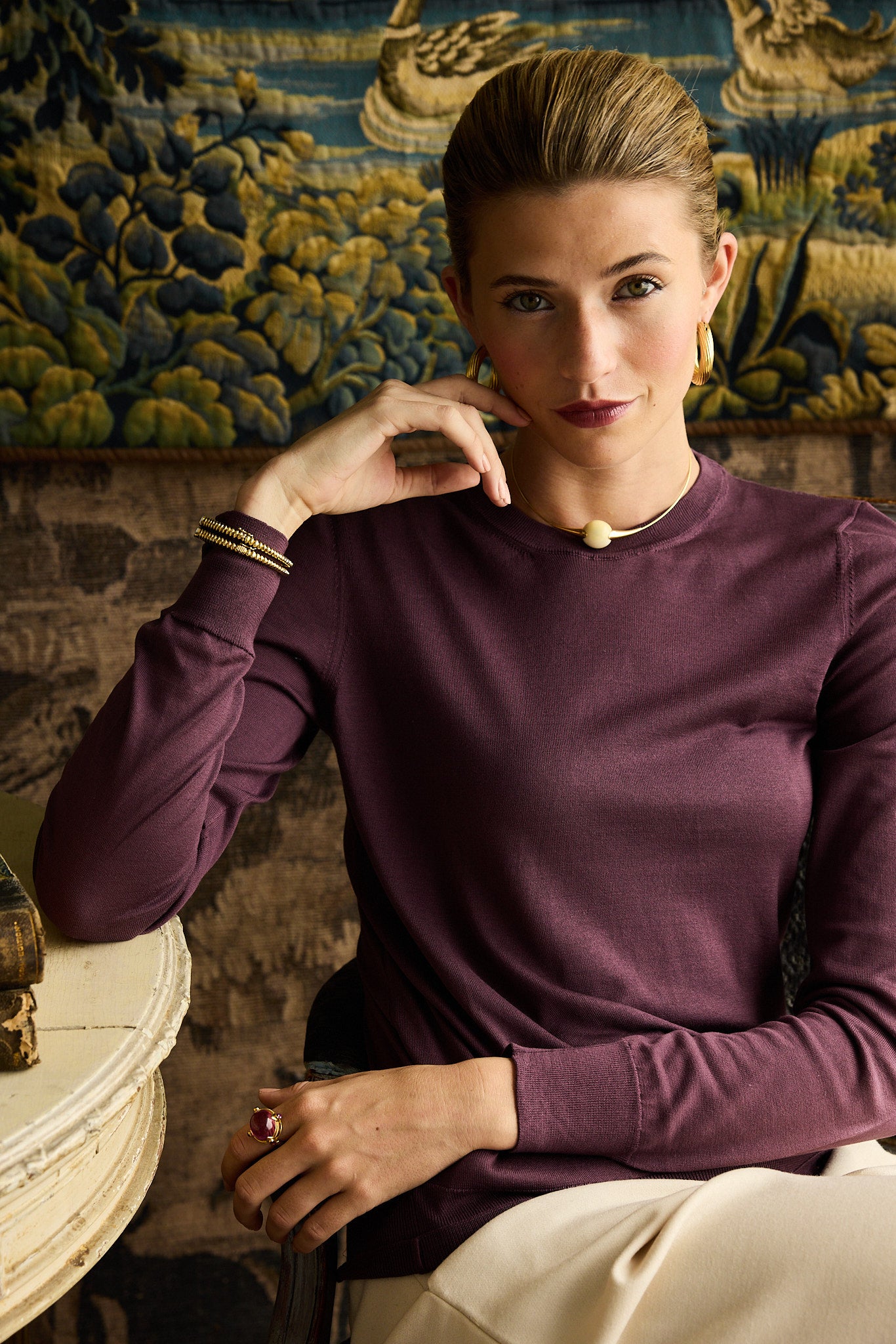 Woman in a purple sweater sitting in a decorative room with tapestries.