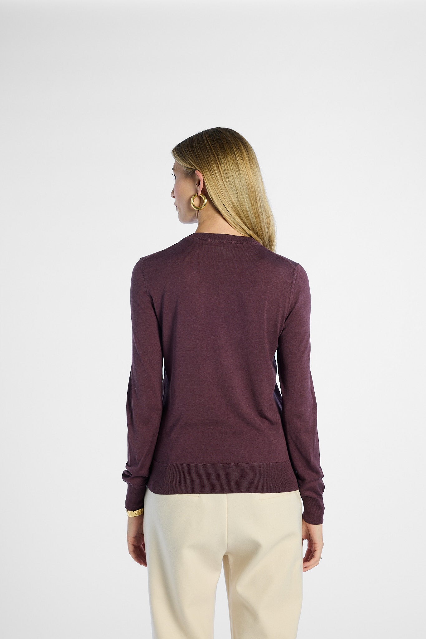 back profile of a Woman wearing a purple sweater and beige pants on a white background