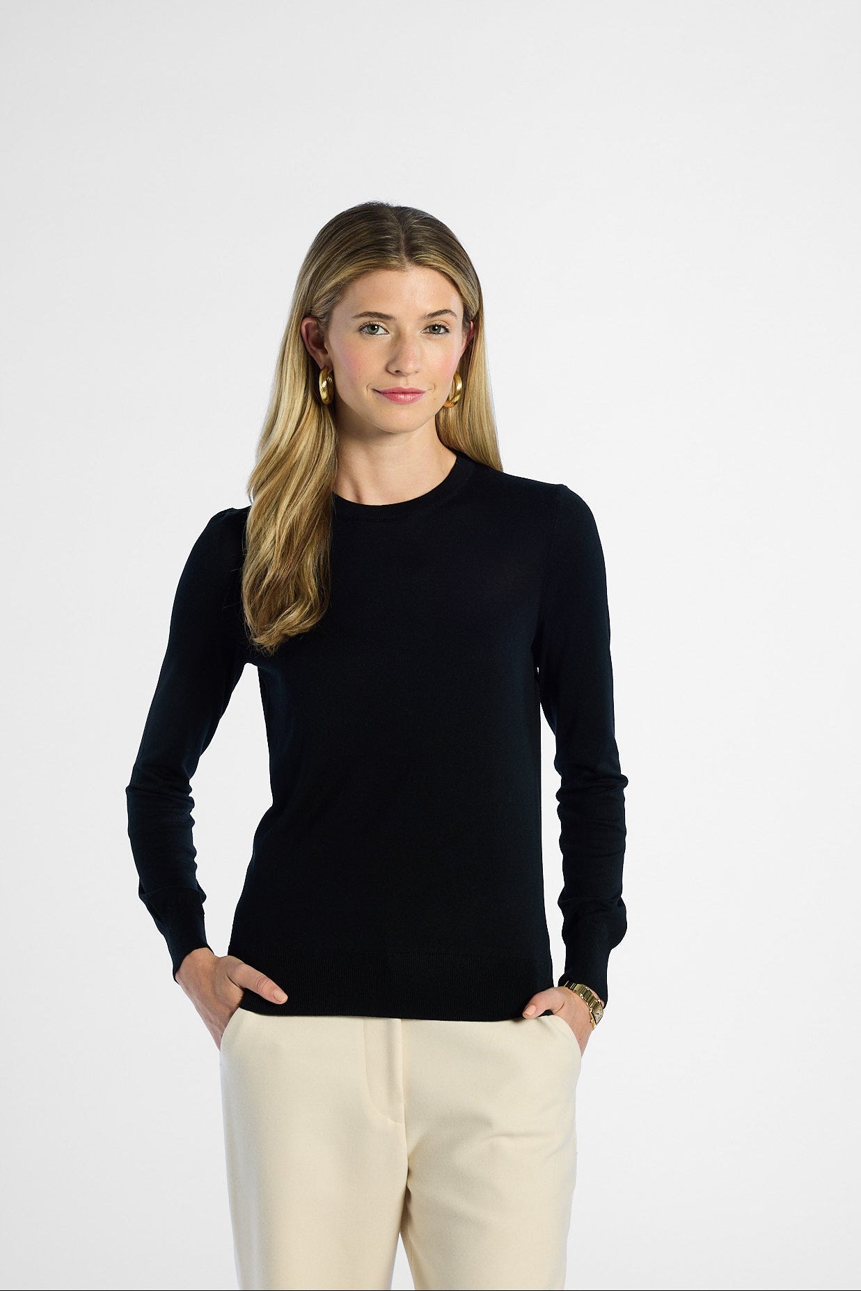 Woman wearing a black long-sleeve top and beige pants on a white background