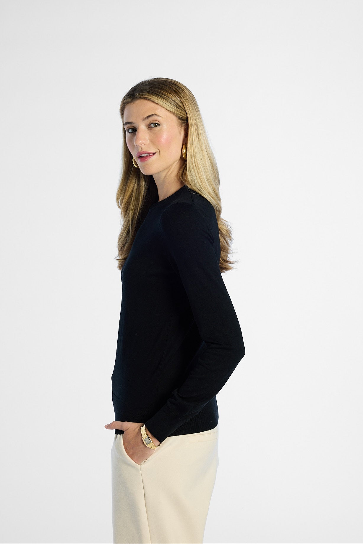 side profile of a woman wearing a black silk crewneck and beige pants on a white background
