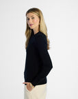 side profile of a woman wearing a black silk crewneck and beige pants on a white background
