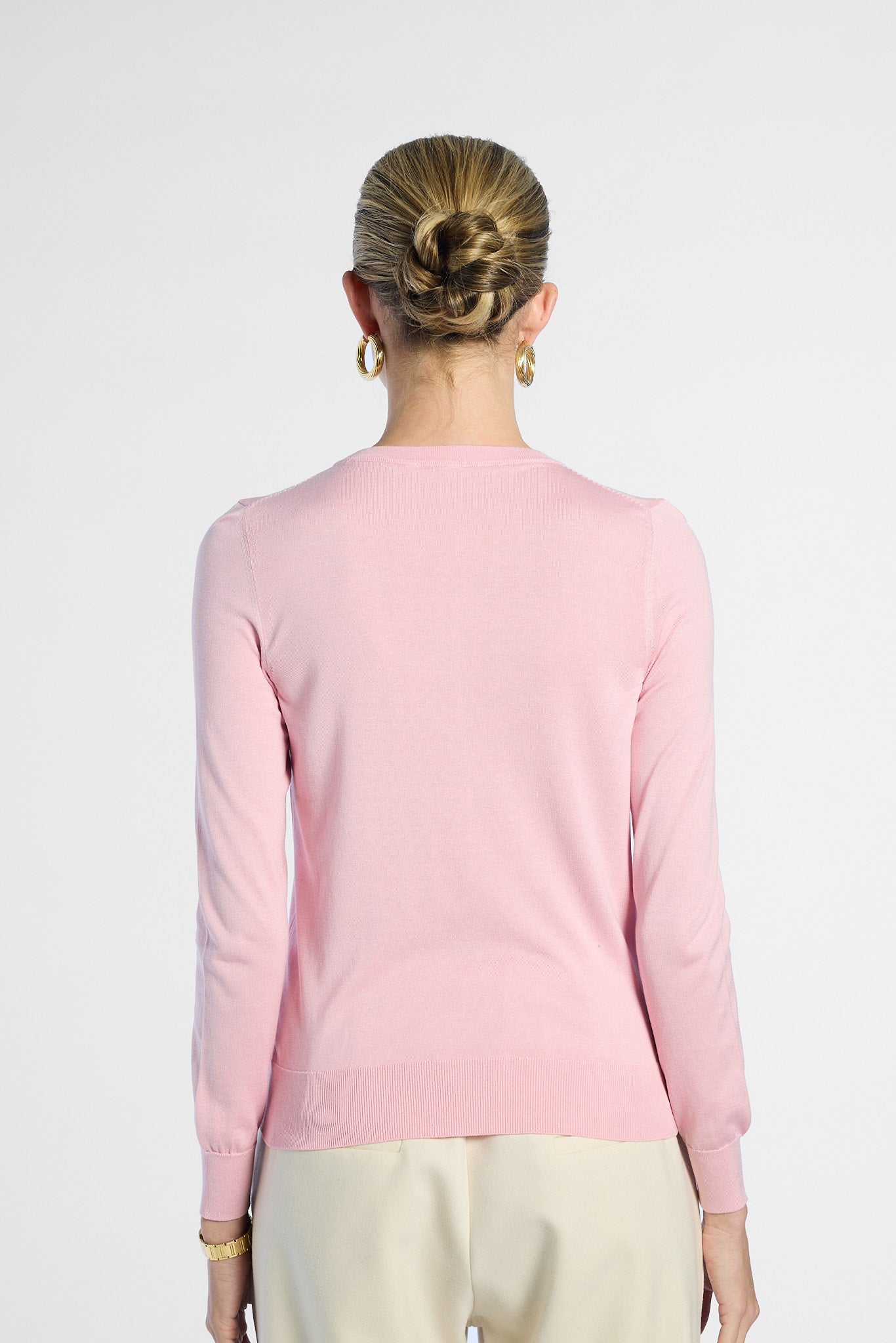 Person wearing a pink silk sweater with a plain background