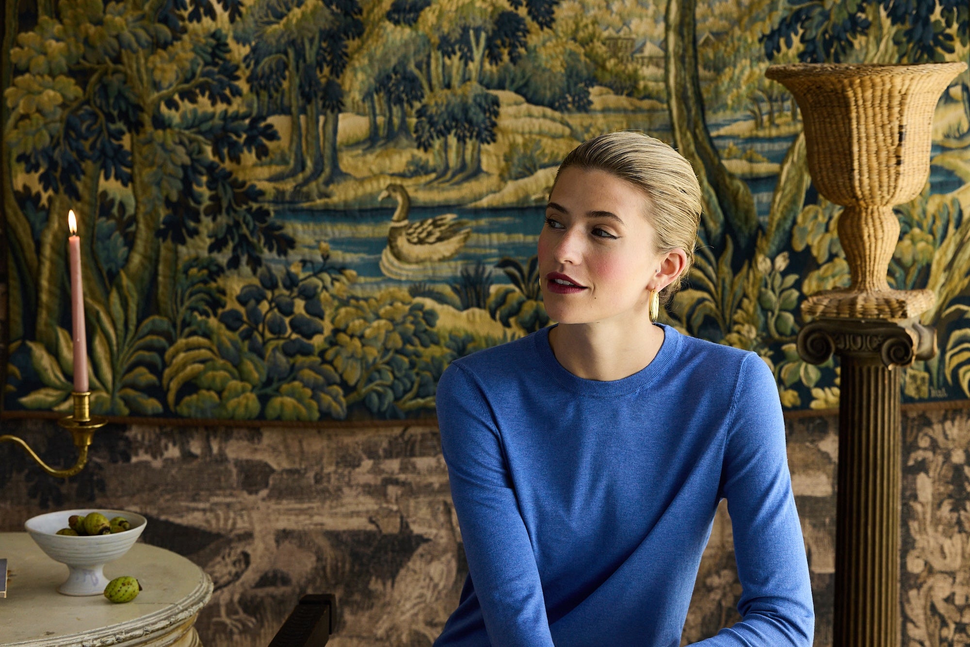 Woman in a blue Silk crewneck sitting in a room with decorative wall tapestry