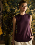 Woman wearing a purple sleeveless top and beige pants standing in front of a decorative wall.