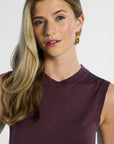 Woman wearing a sleeveless silk purple top against a plain background
