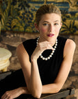 Woman in a black silk shell with a pearl necklace against a decorative wall.
