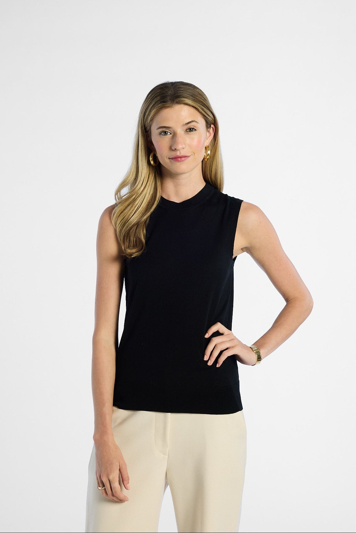 Woman wearing a black sleeveless silk top and beige pants on a white background