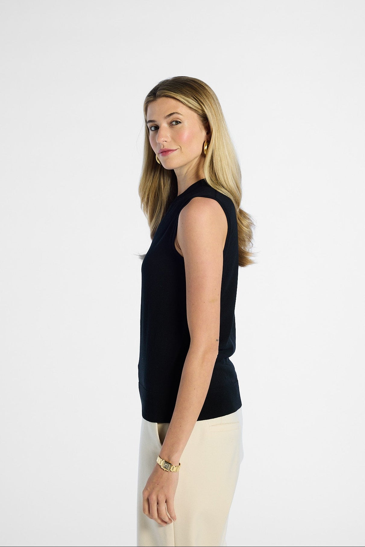 side profile of a Woman wearing a black sleeveless silk top and beige pants on a white background