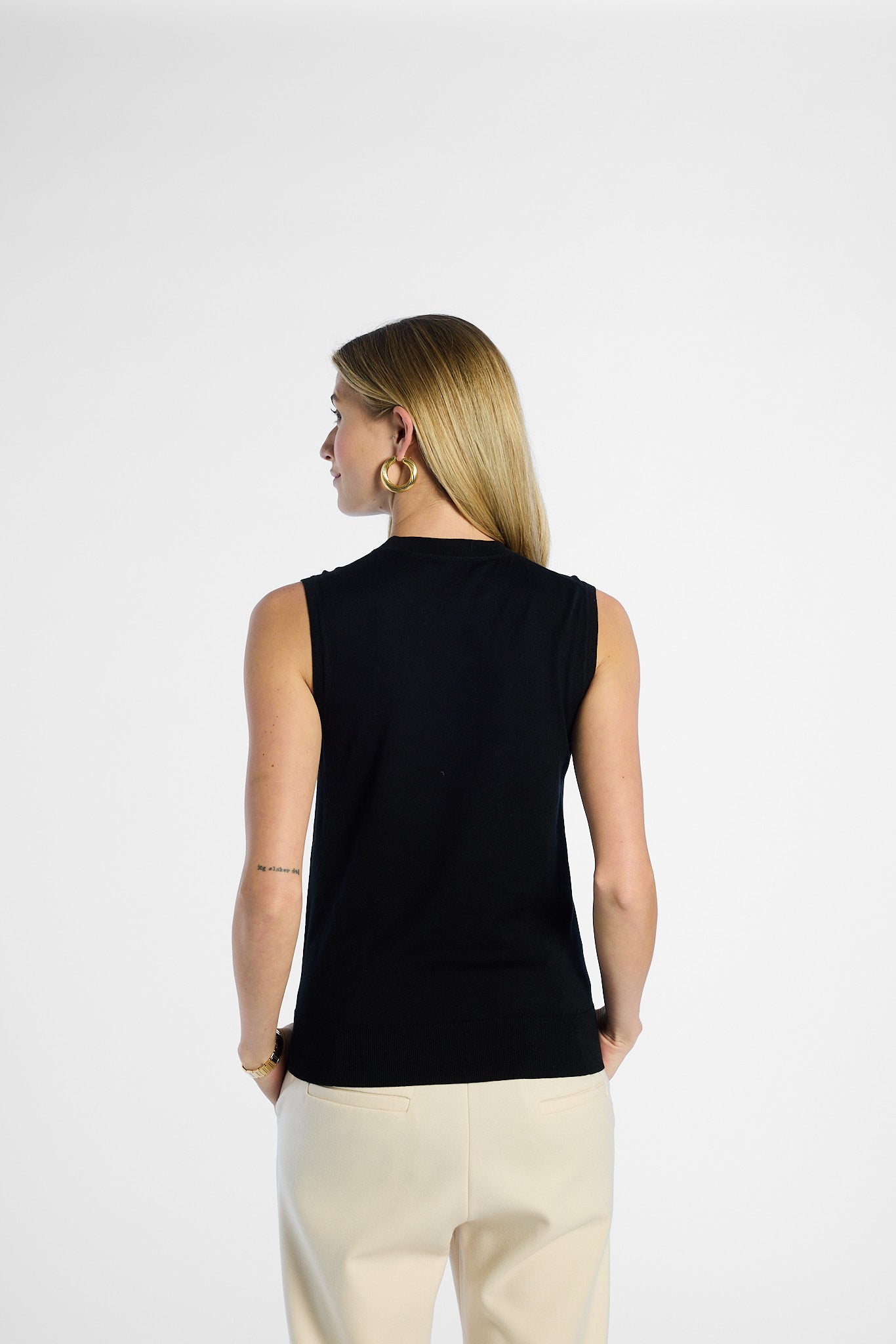 Woman wearing a black sleeveless top and beige pants on a white background