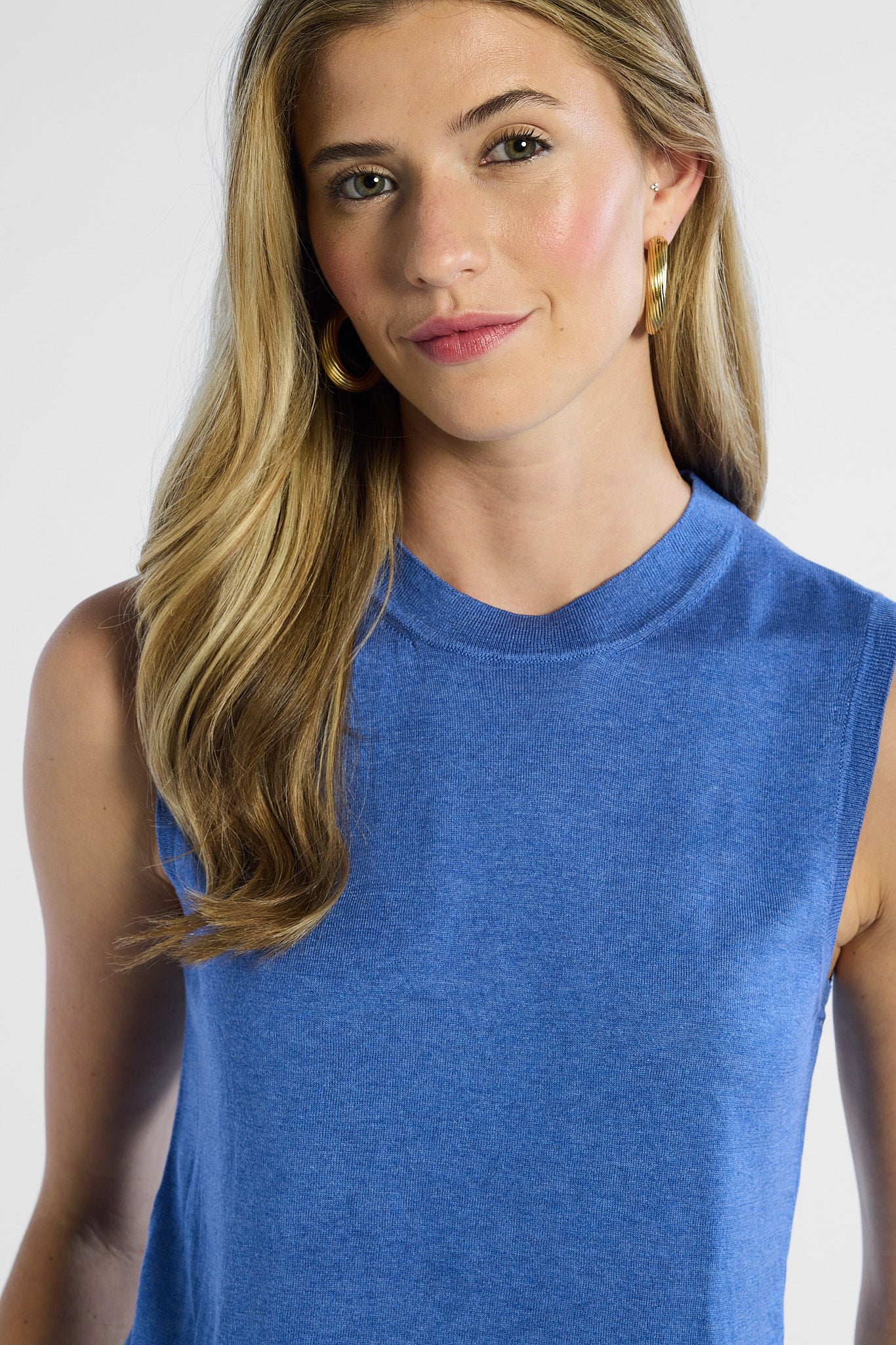 Woman wearing a blue sleeveless silk top against a white background