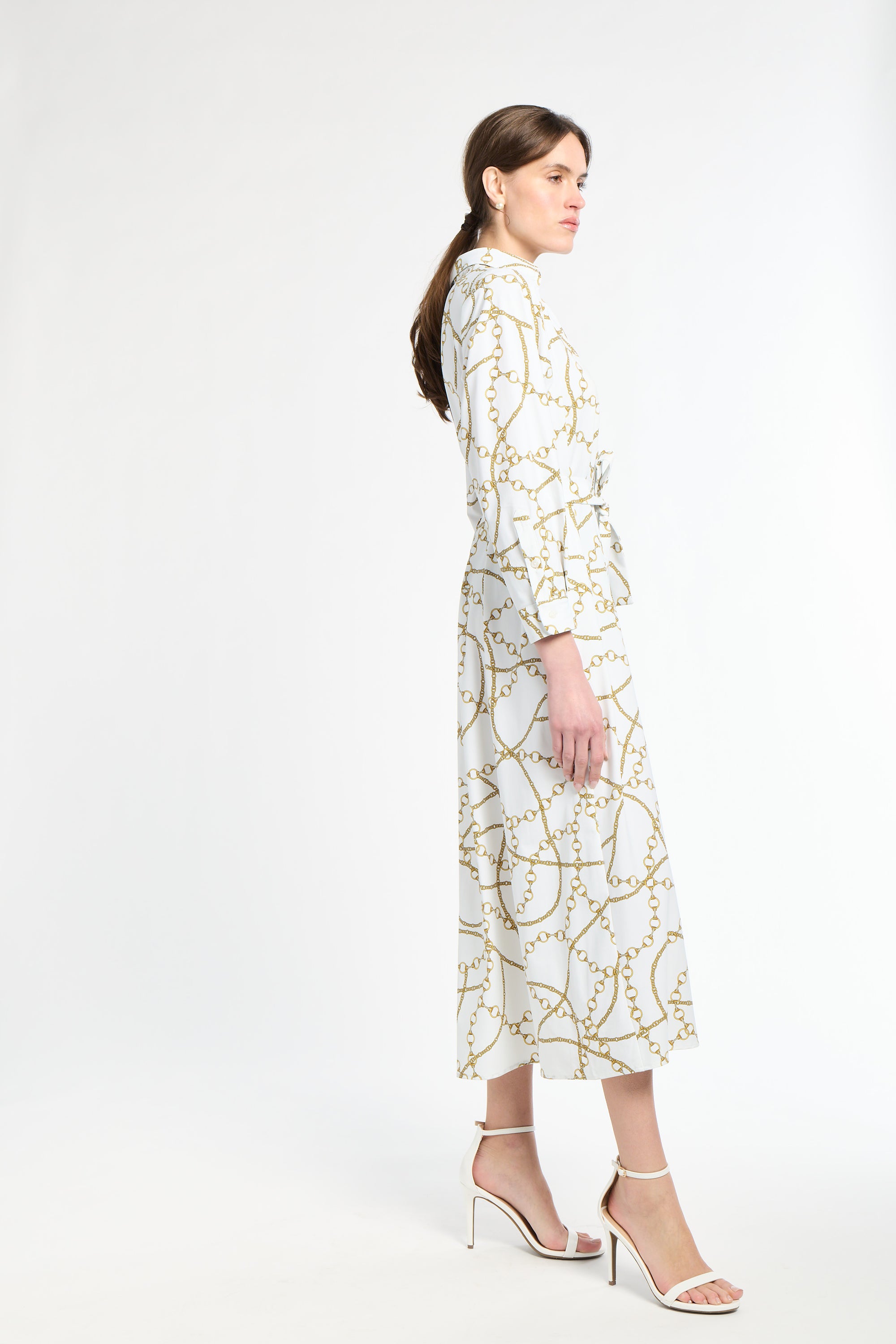 Woman wearing a white dress with gold pattern and white heels on a white background
