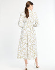 Woman wearing a long sleeve white dress with a gold chain pattern on a white back drop