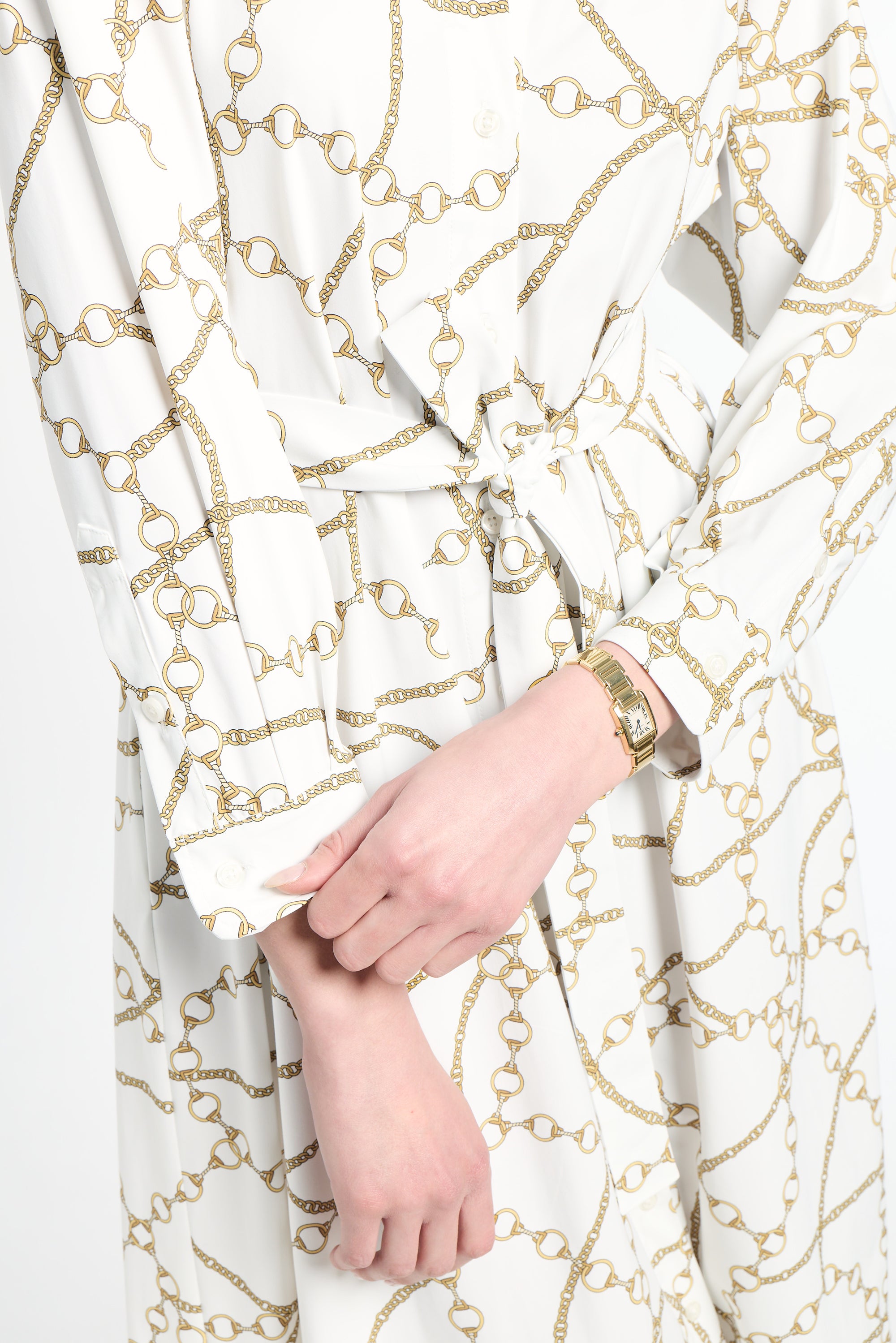 Close-up of a white garment with gold chain pattern and a hand wearing a gold watch