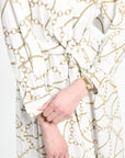 Close-up of a white garment with gold chain pattern and a hand wearing a gold watch