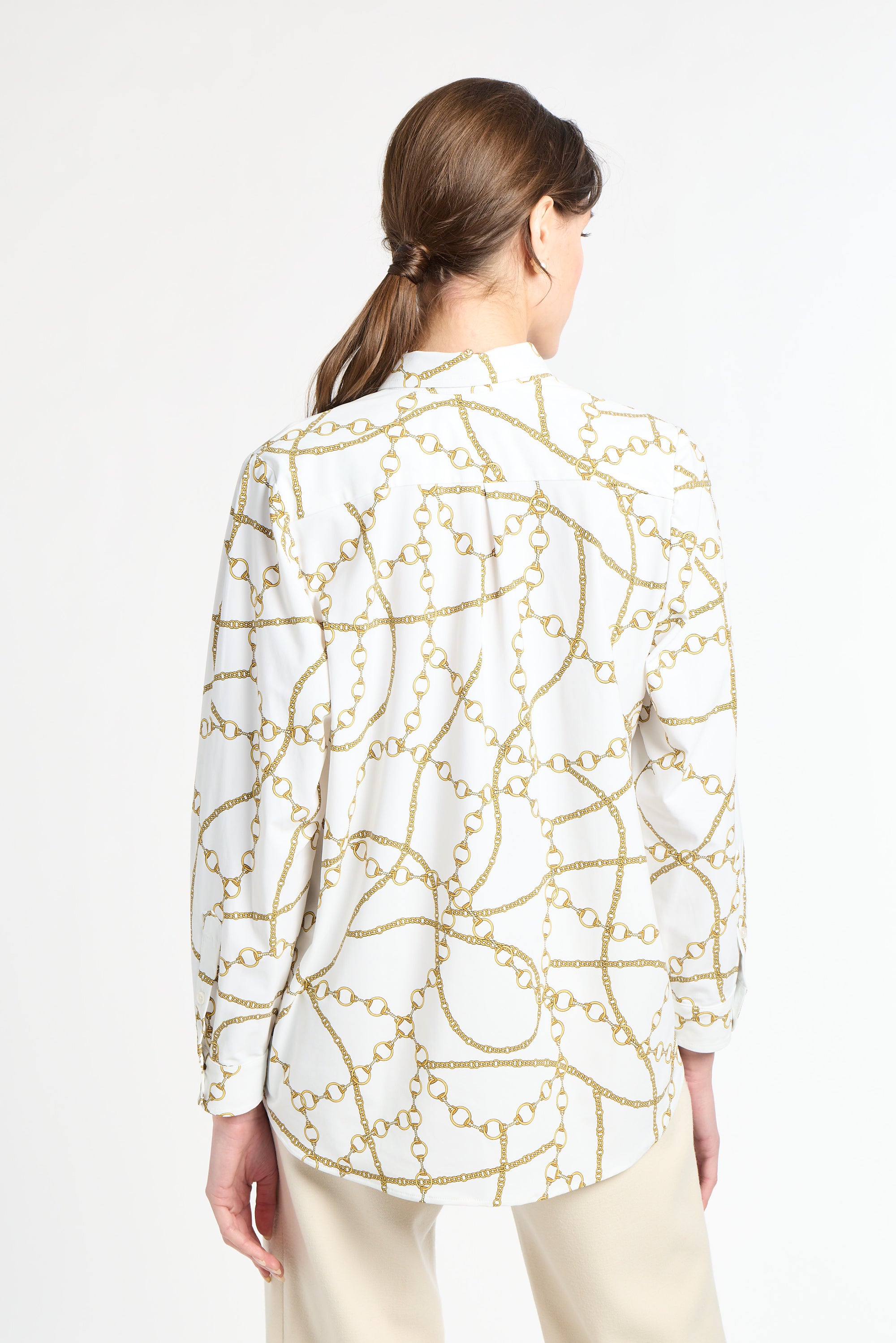 Woman with her back wearing a white and gold blouse with khaki pants