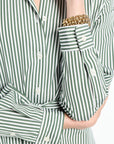 Green and white striped shirt with a gold bracelet on a plain background