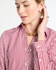 Woman wearing a red and white striped shirt with gold jewelry on a plain background