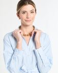 Woman wearing a light blue striped shirt and gold necklace on a white background