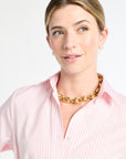 Woman wearing a pink striped shirt and gold necklace against a white background