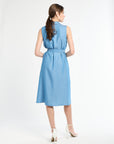 Woman with dark hair modeling blue dress  and wearing white heels against white backdrop
