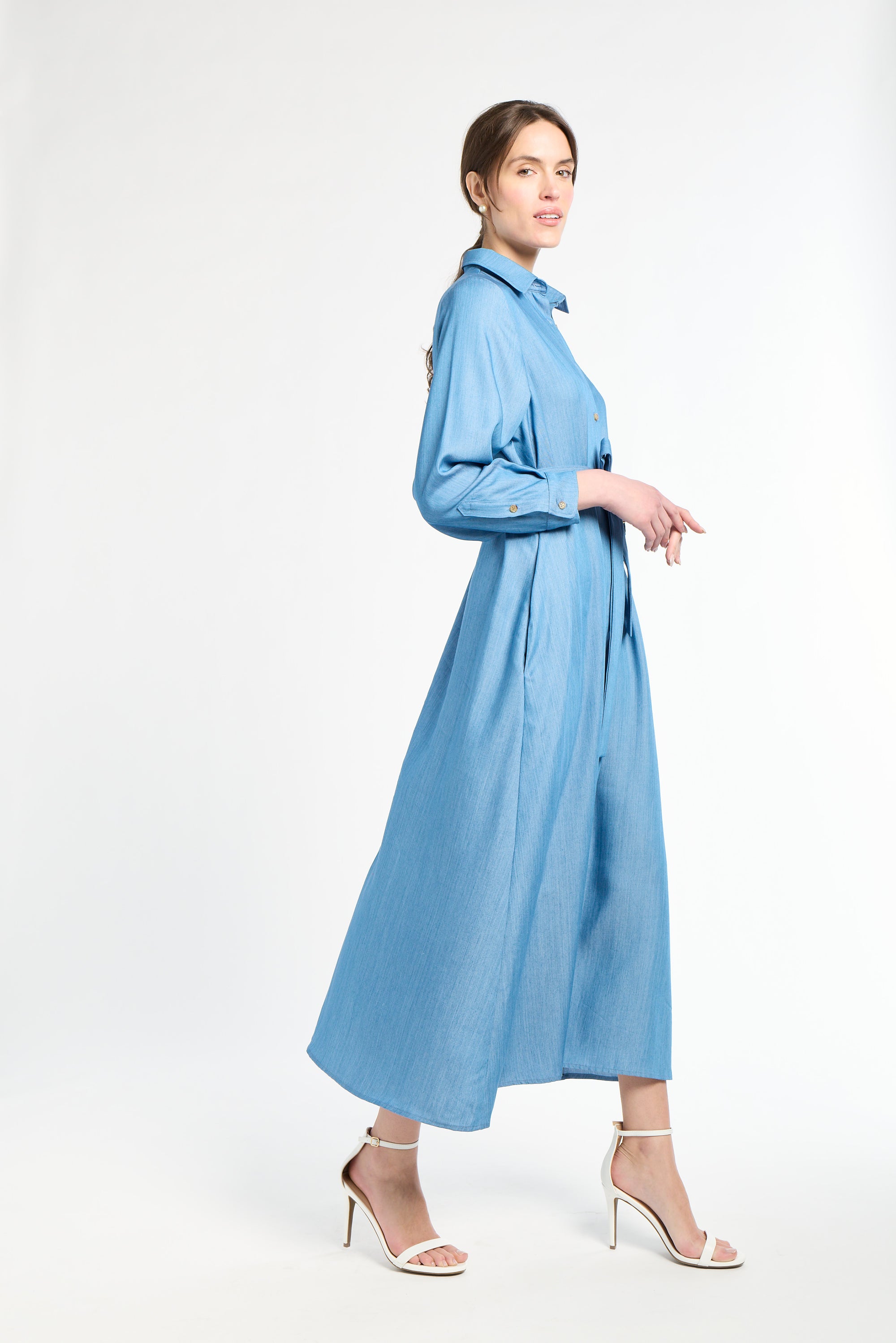 Woman wearing a long blue dress and white heels on a white background