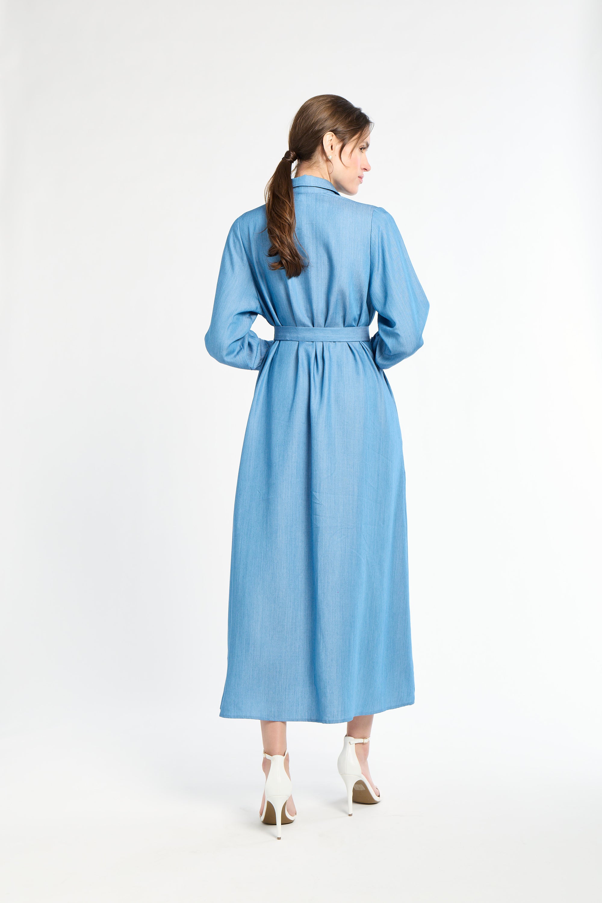 Woman standing modeling a long blue dress against a white background