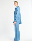 Woman standing sideways modeling a blue blouse and pants on a white backdrop