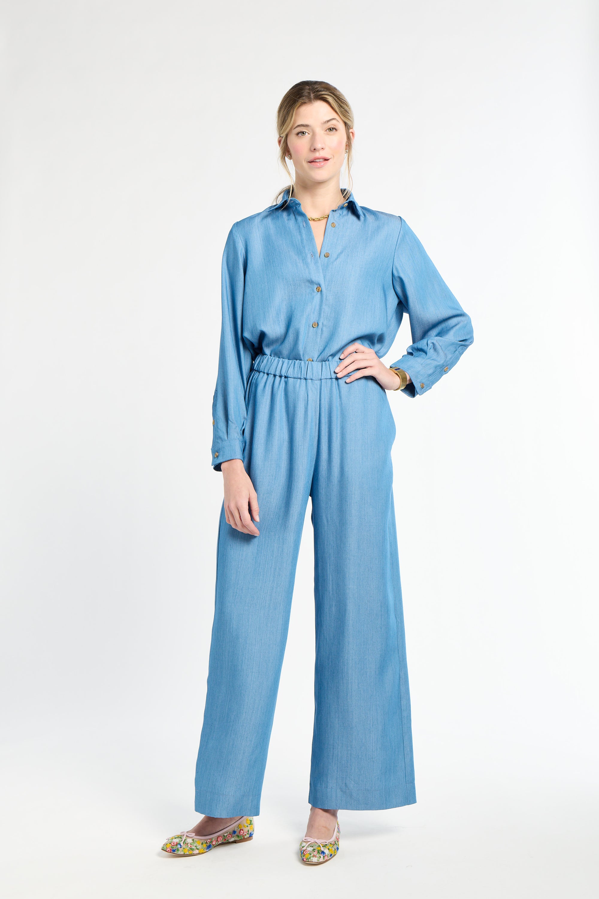 Woman modeling blue pants on a white background with hand on hip