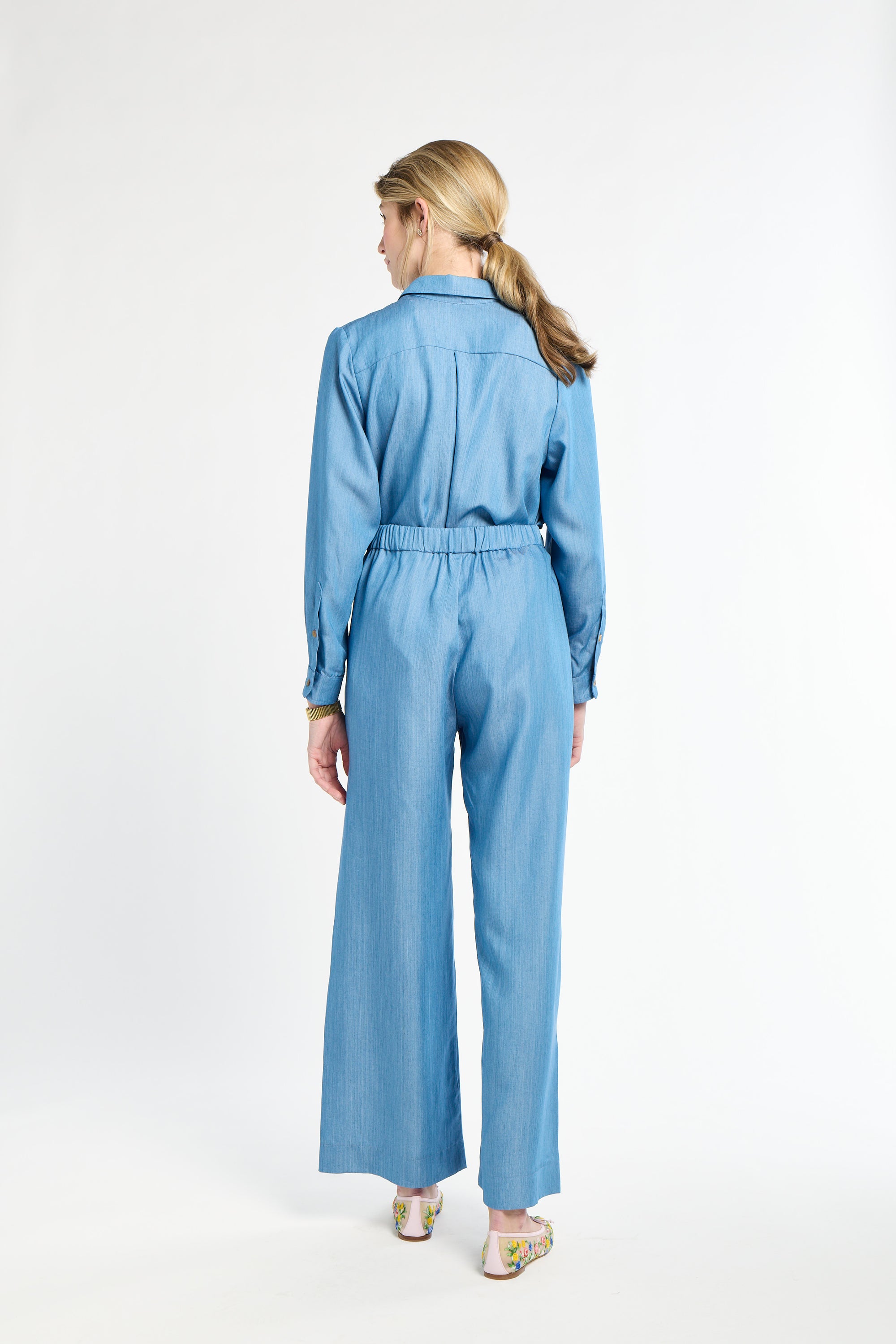 Woman modeling blue pants and long sleeve shirt against a white background