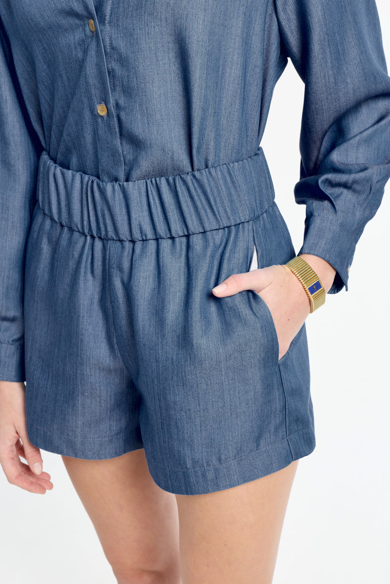 Person wearing a blue denim romper on a white background
