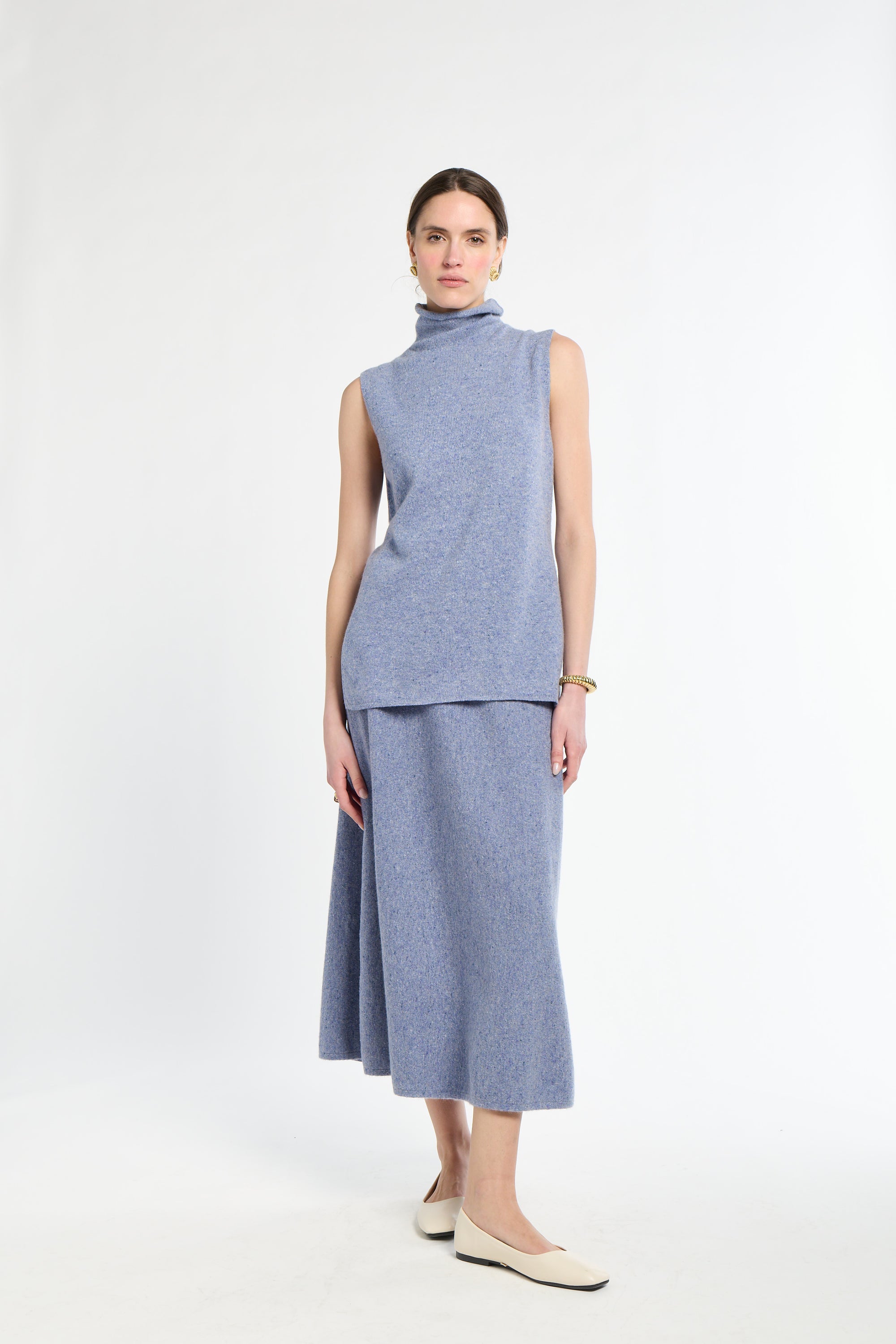 Woman with sleeveless blue sweater on with matching blue knit skirt. 