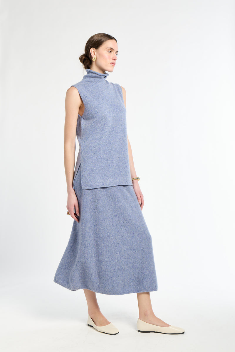 Woman wearing light blue sleeveless sweater with matching light blue knit skirt. 