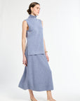Woman wearing light blue sleeveless sweater with matching light blue knit skirt. 
