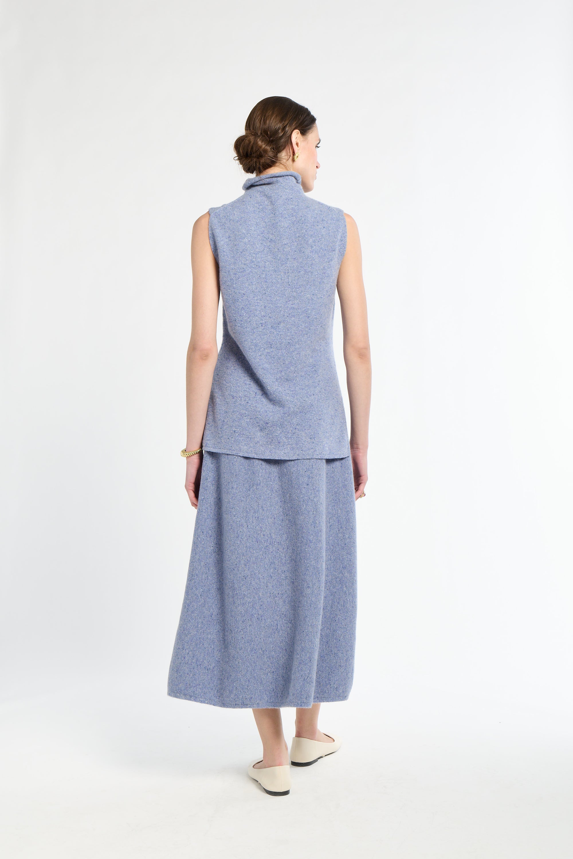 Woman wearing light blue sleeveless sweater with matching light blue knit skirt. 