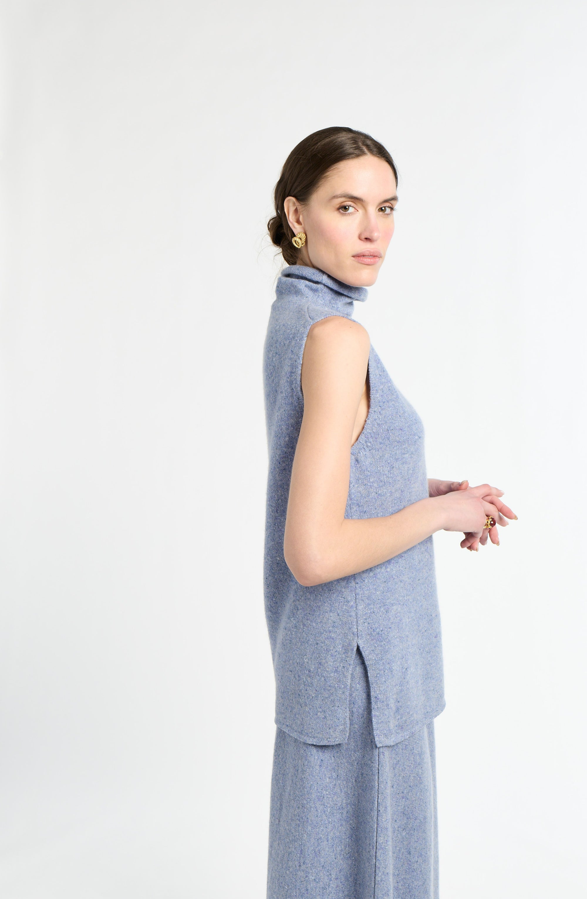 Woman with blue sleeveless knit on with white background. 