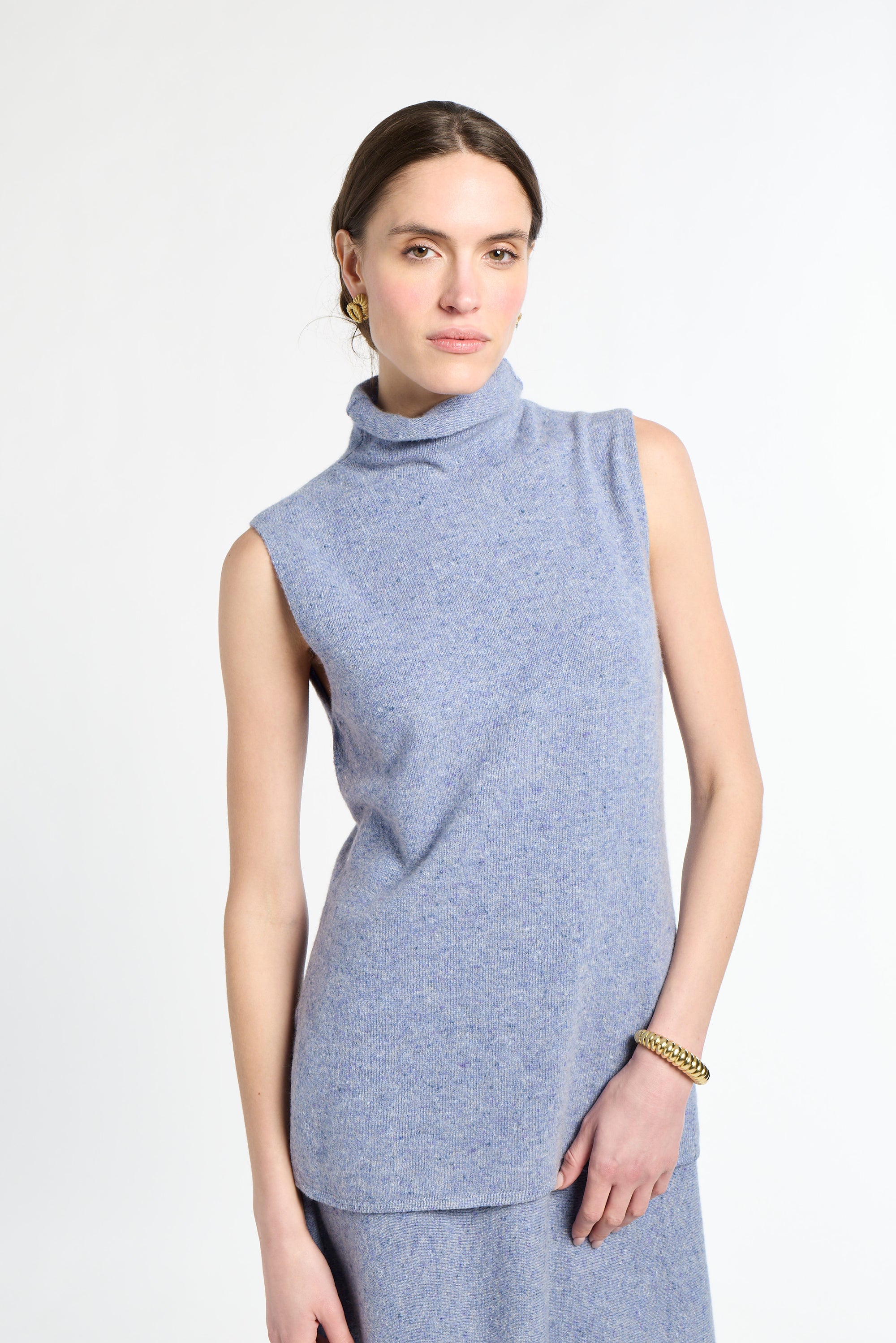 Woman with blue sleeveless knit on with white background. 