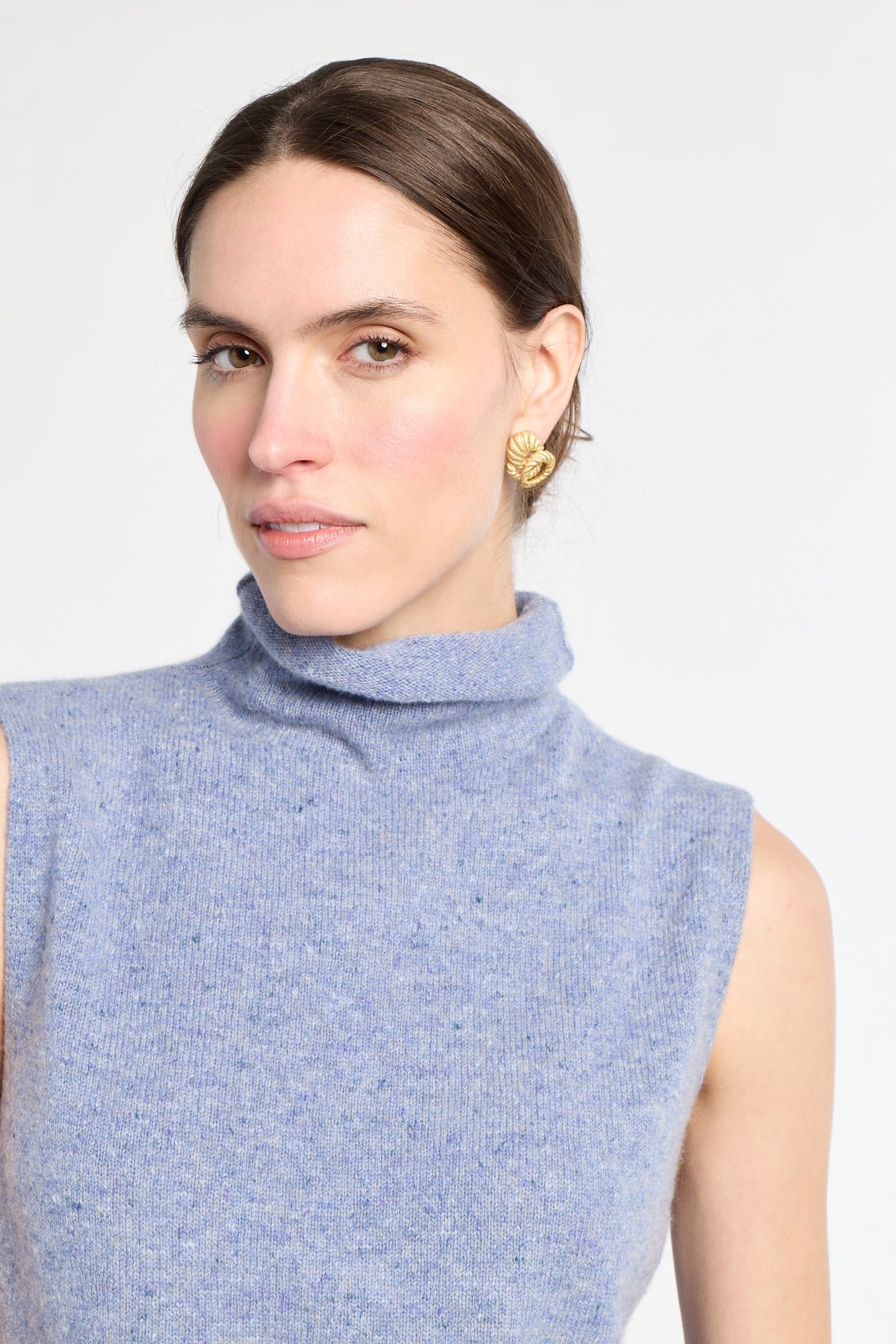 Woman with blue sleeveless knit on with white background. 