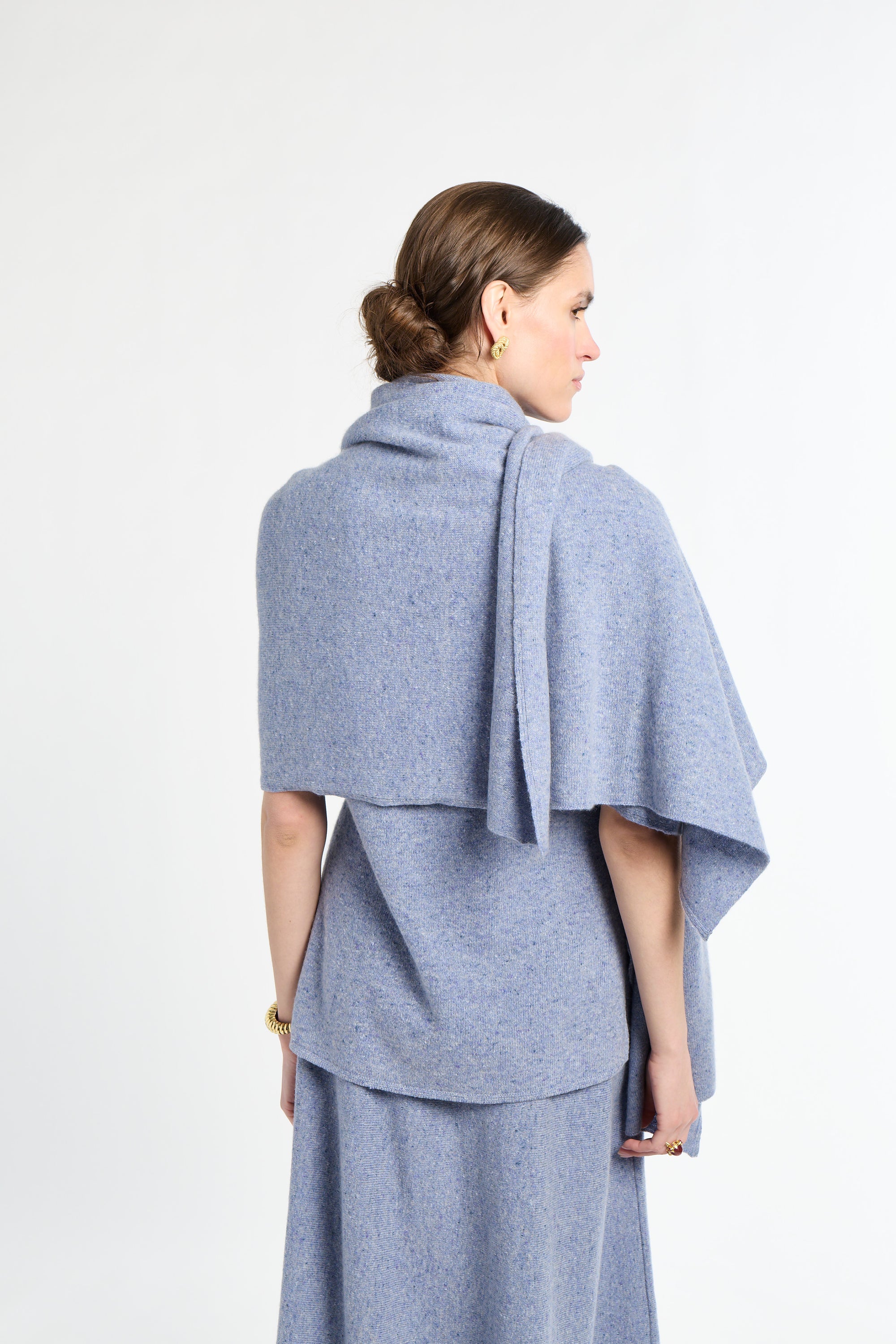 Woman wearing a light blue poncho over a dress on a white background