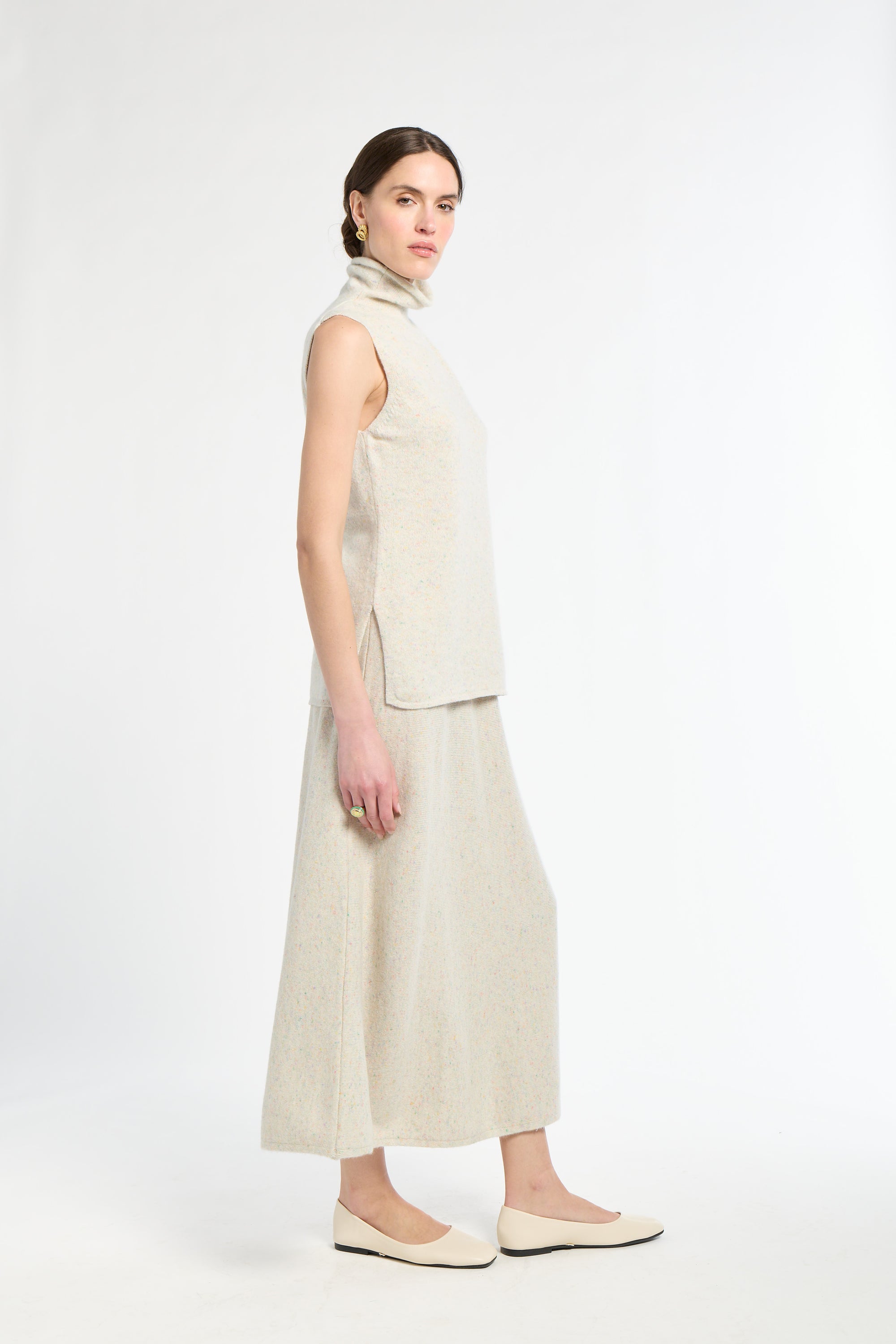 Woman wearing a beige sleeveless top and high-waisted pants on a white background