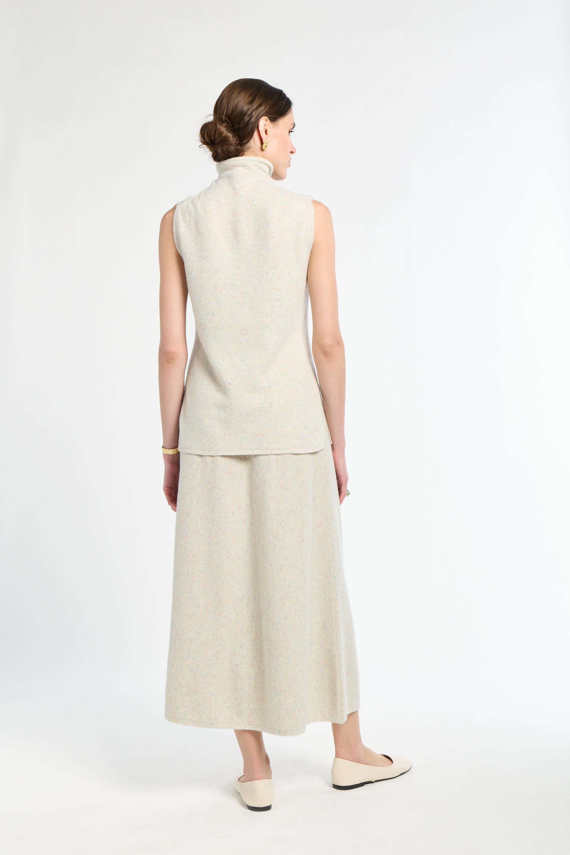 Woman wearing a sleeveless beige top and long skirt on a white background