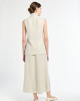 Woman wearing a sleeveless beige top and long skirt on a white background