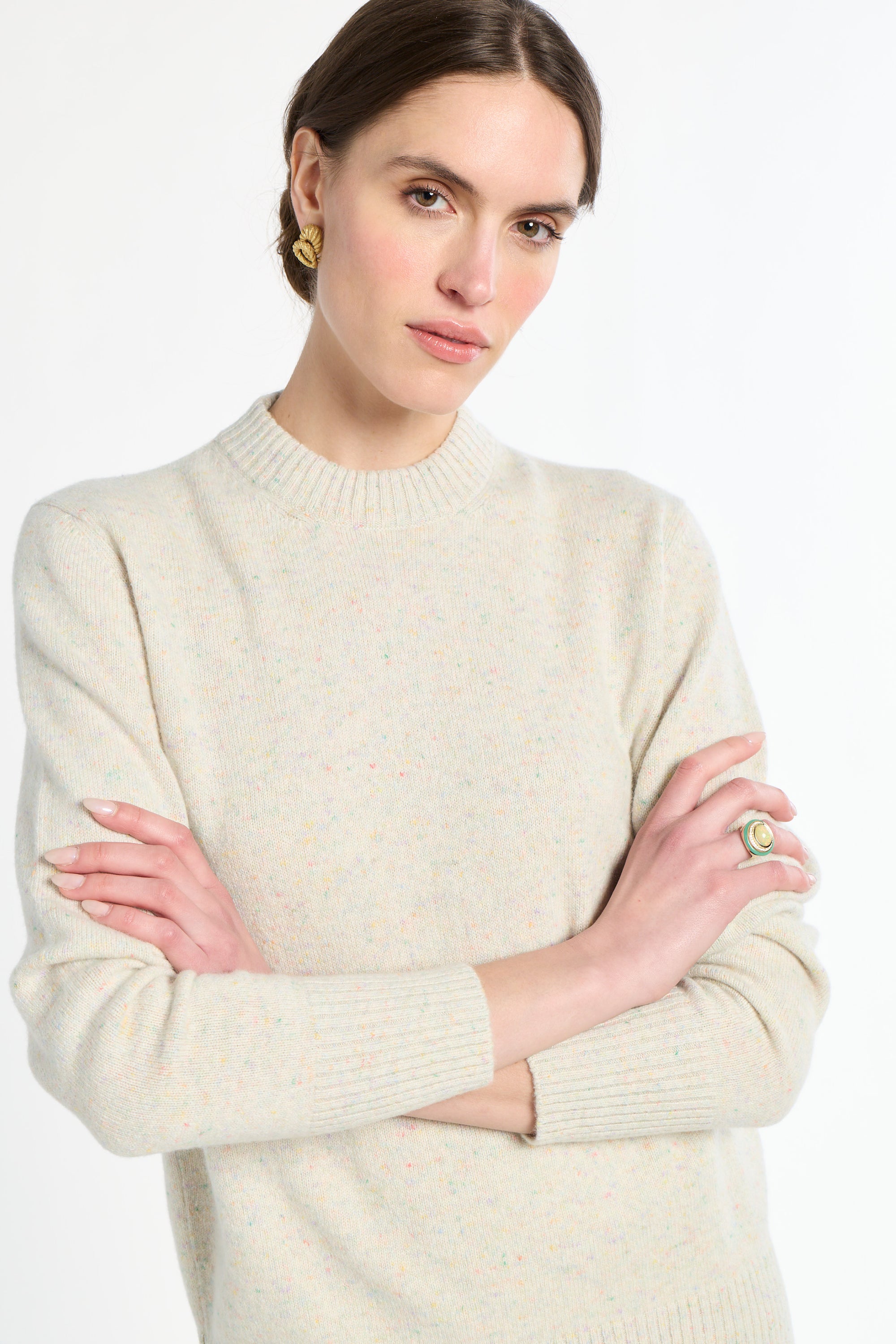 Woman wearing a cream sweater with arms crossed on a white background