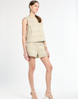 Woman wearing a golden and light blue sleeveless tweed shirt and shorts on a white background